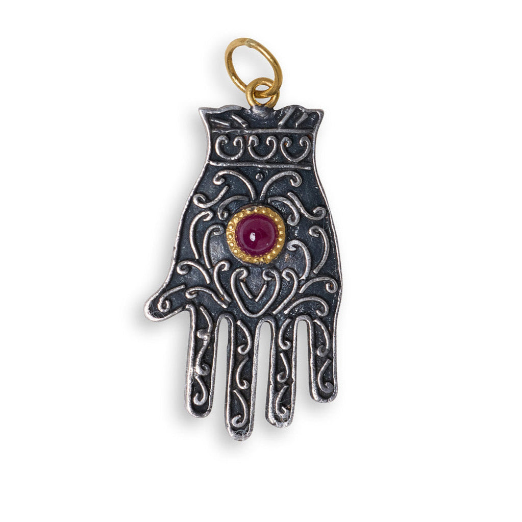 Decorative hand-shaped pendant with a red gemstone on a white background