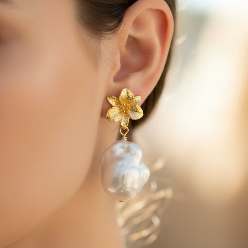 Pearl earrings with gold flower-like attachments on a white background