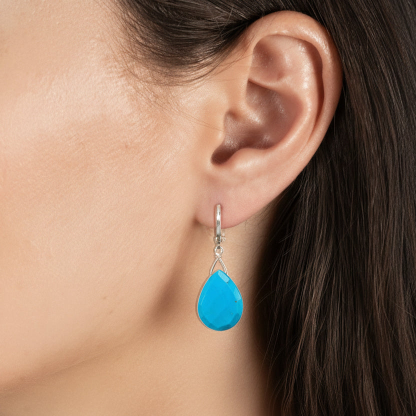 Close-up of an ear wearing a turquoise teardrop earring with a blurred background