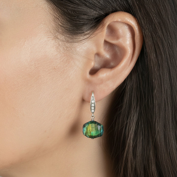Close-up of an ear wearing a dangling earring with a clear gemstone.