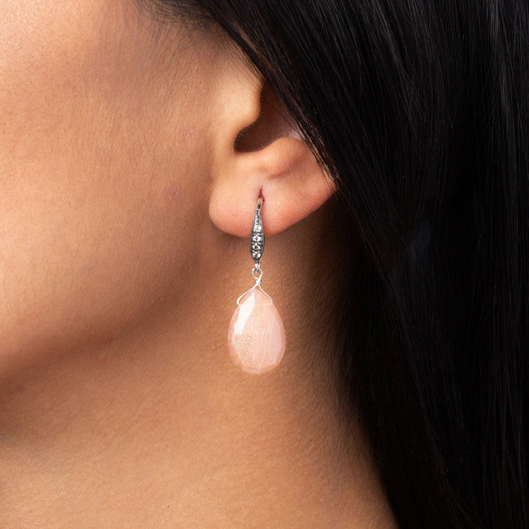 Close-up of a person wearing a pink teardrop earring with a blurred background