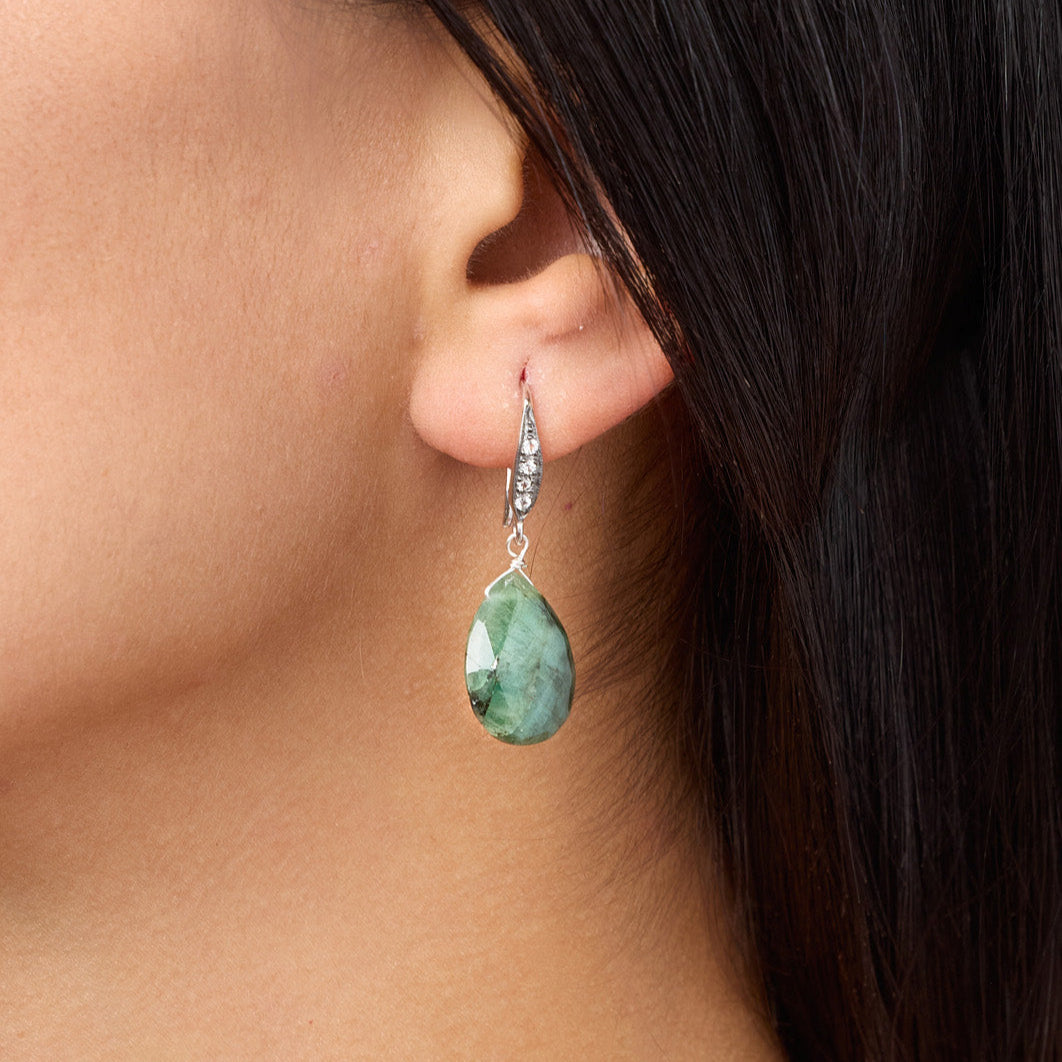Close-up of a person wearing a teardrop-shaped green gemstone earring.