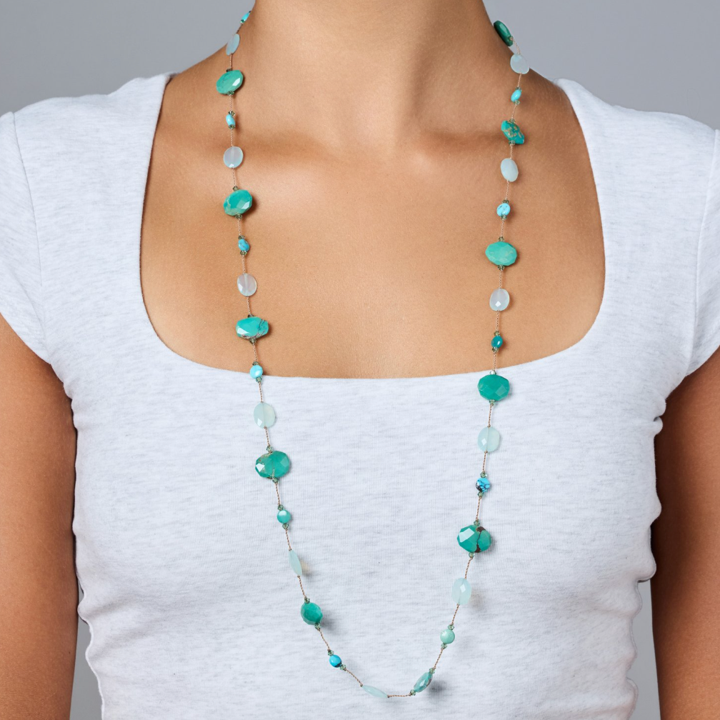 Woman wearing a long turquoise beaded necklace against a gray background